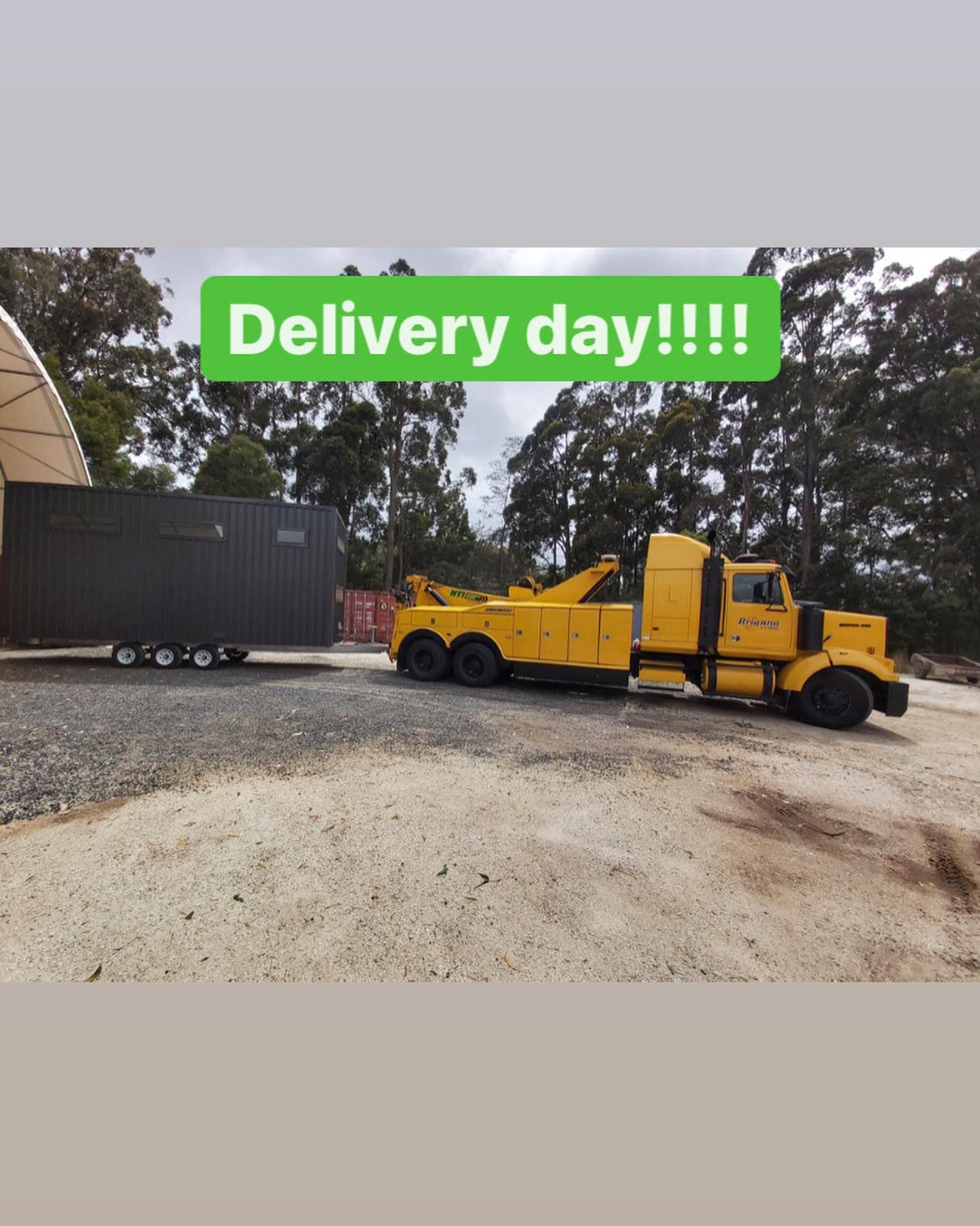 A yellow tow truck is carrying a container on a trailer.