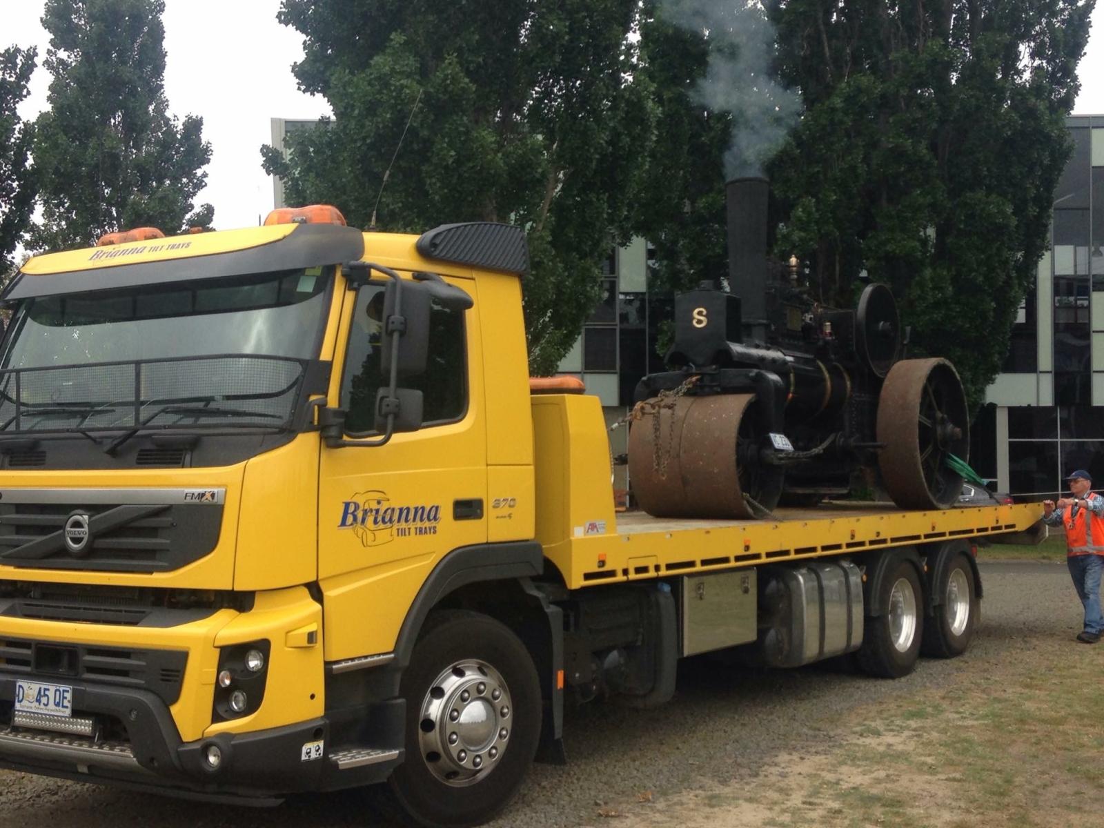 24/7 truck recovery hauling old steam engine with safety crew on gravel lot.