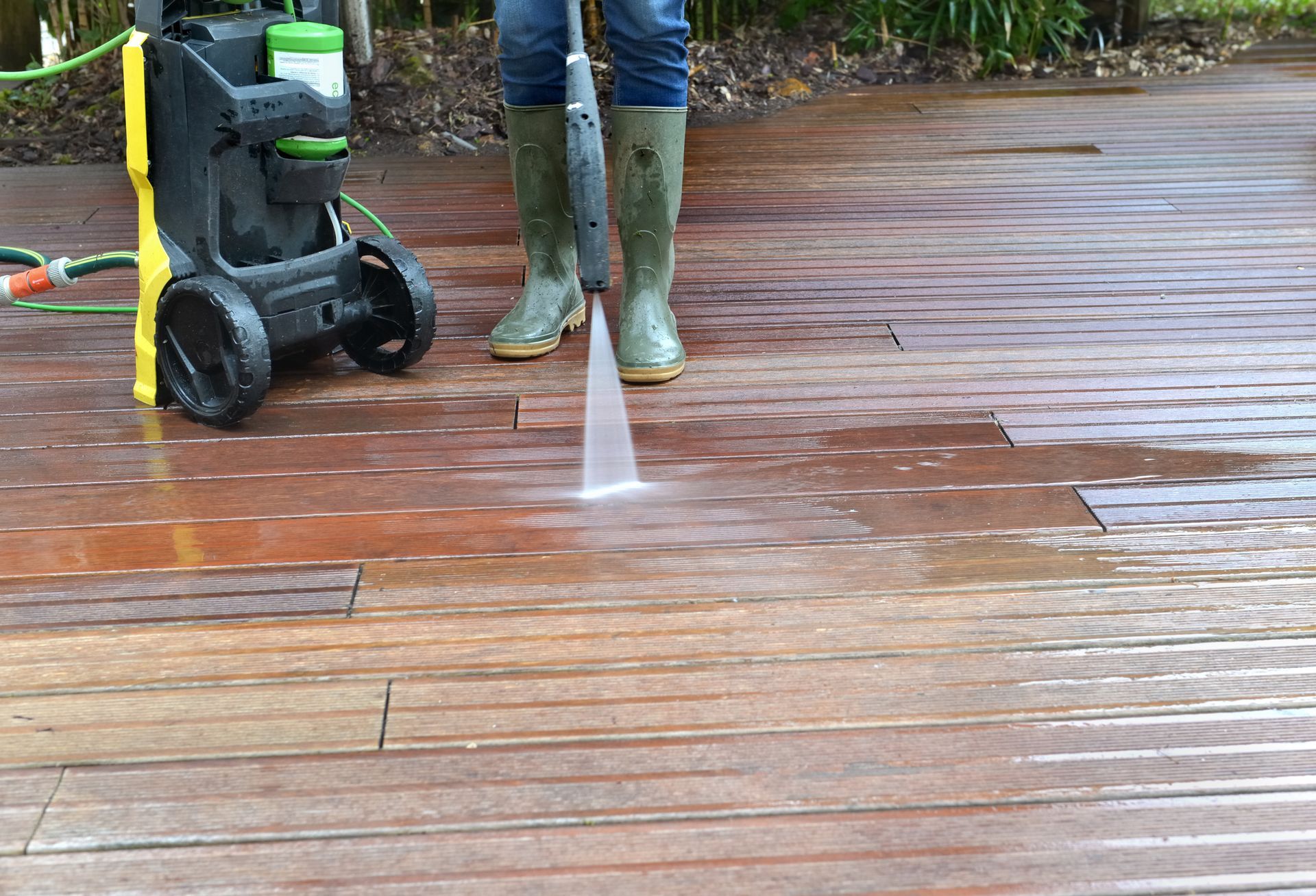 Closeup of person using a power washer on wooden floor, showcasing power washing company services.