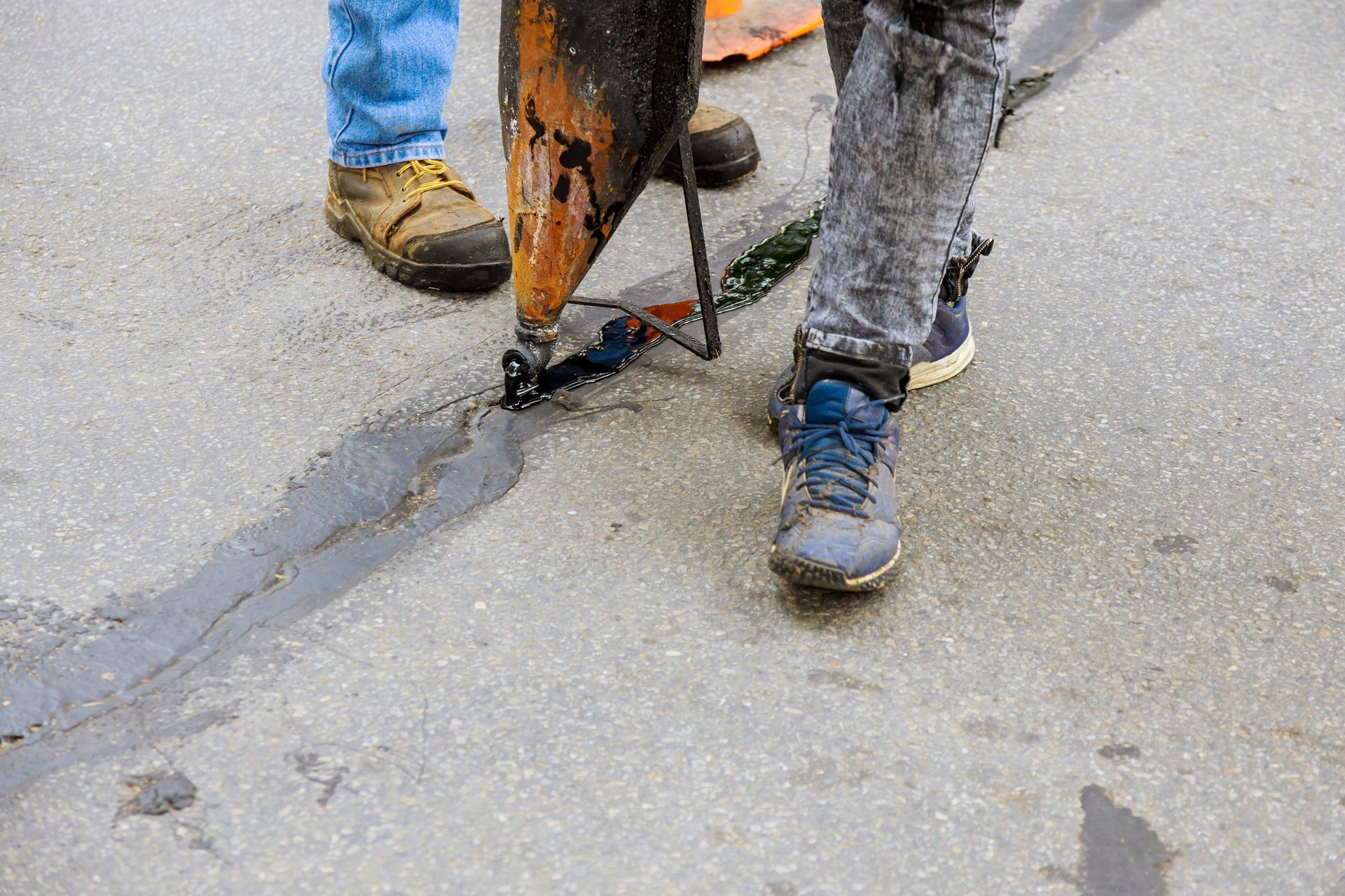 Workers sealing asphalt crack with hot tar on roadway surface during pavement repair process.
