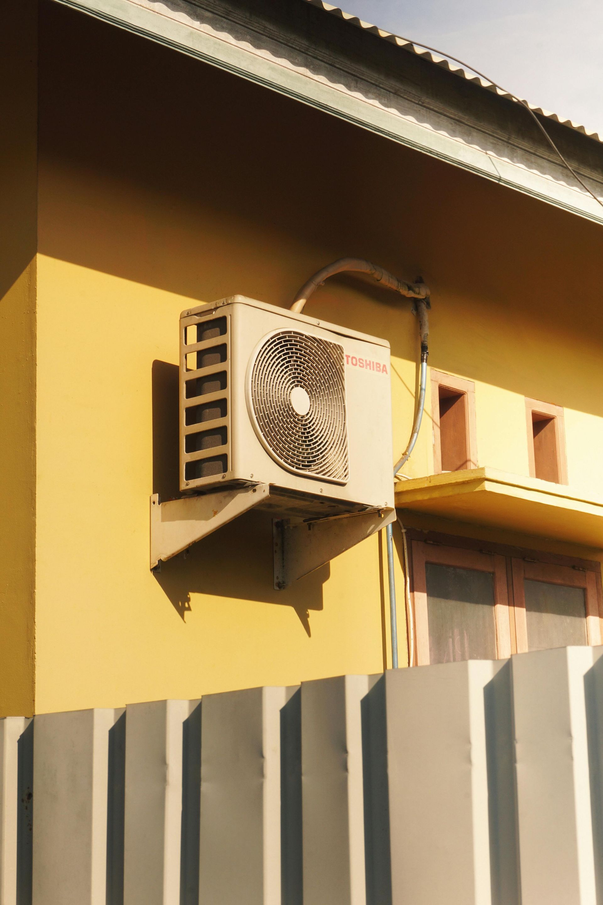 Exterior air conditioning unit mounted on a yellow wall next to a window.