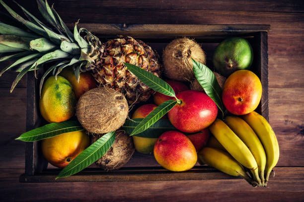 A wooden box filled with tropical fruits on a wooden table.