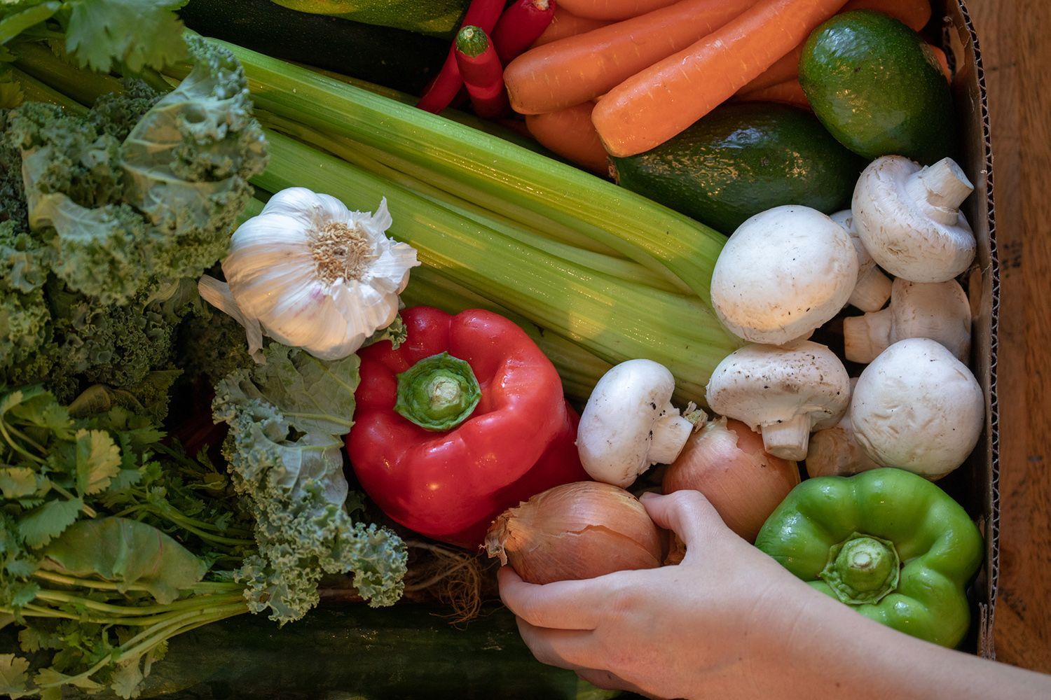 A person is picking an onion from a box of vegetables.