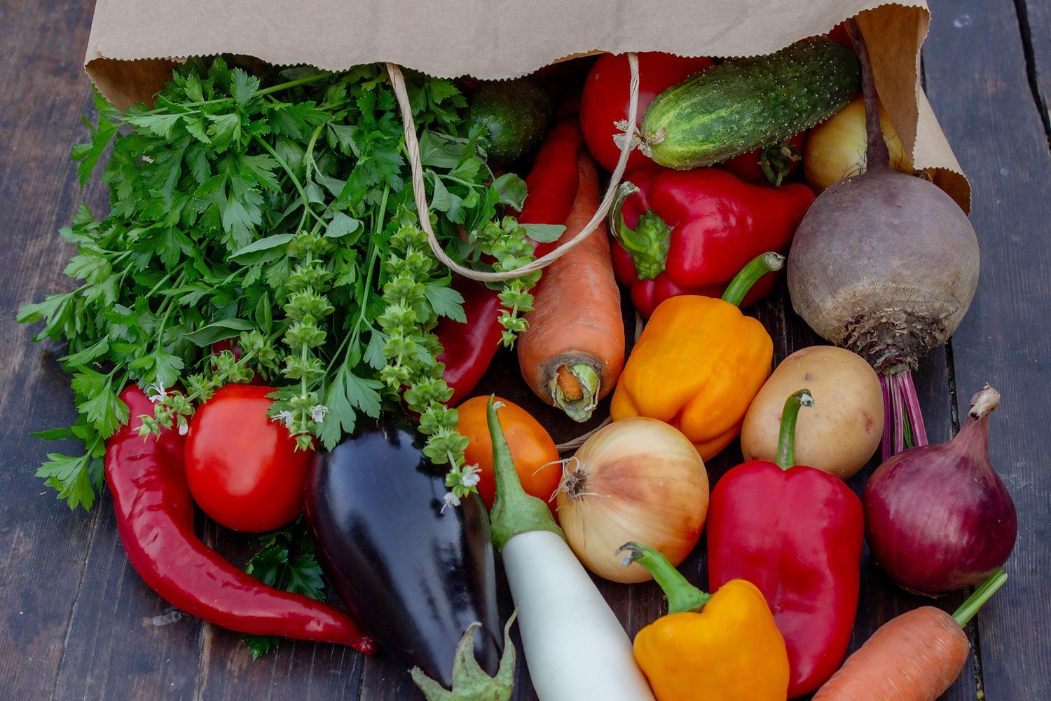 A paper bag filled with vegetables is sitting on a wooden table.