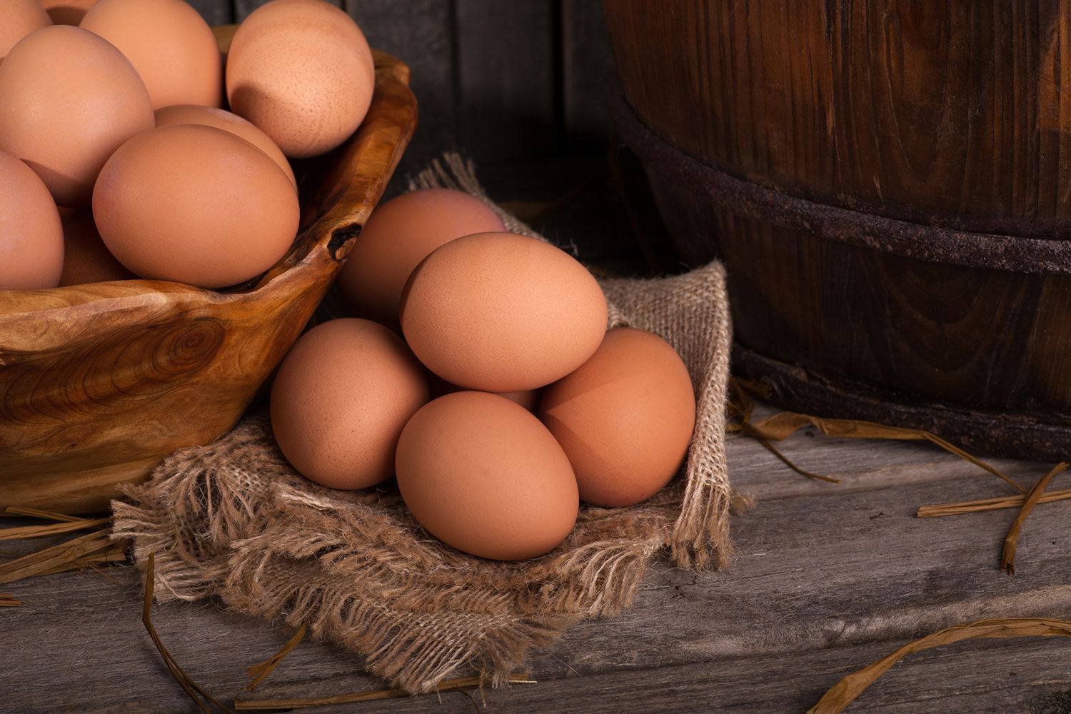 A wooden bowl filled with brown eggs on a wooden table.