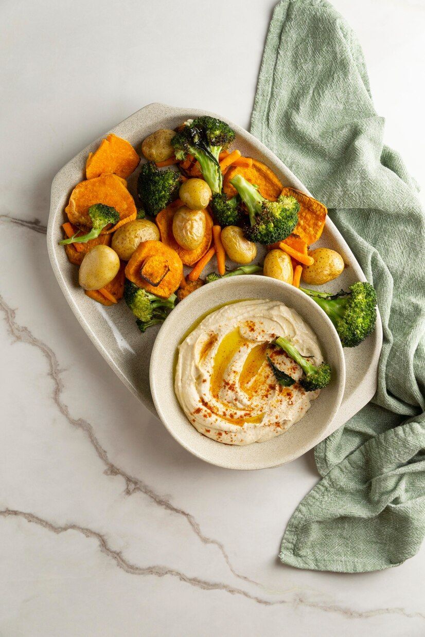 A plate of vegetables and a bowl of hummus on a table.