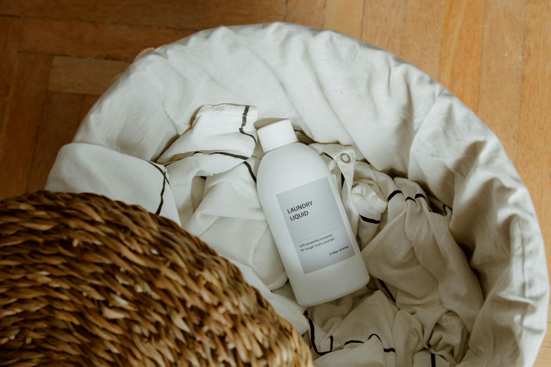 A white plastic bottle with a label sits inside a fabric laundry basket lined with cream-colored, patterned fabric.