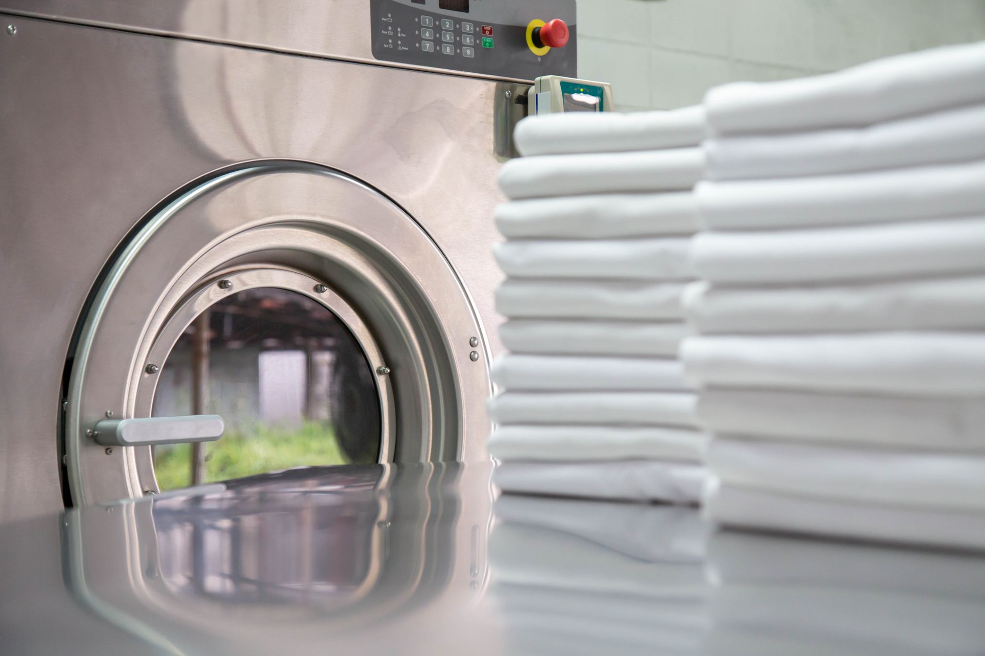 A stack of neatly folded white towels sits on a metal table next to an industrial washing machine.