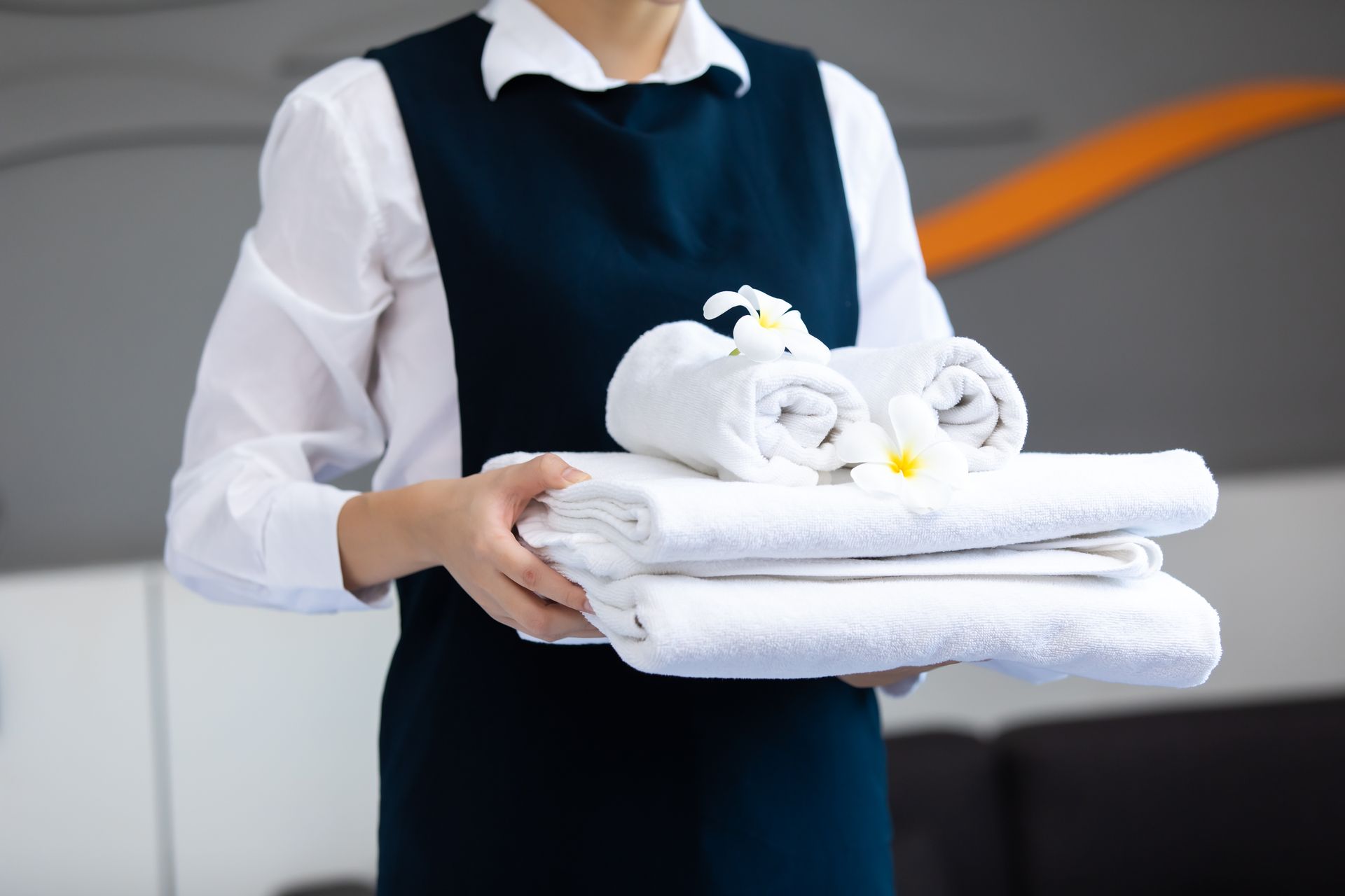 A person in a professional uniform holds a stack of folded white towels adorned with two white flowers.