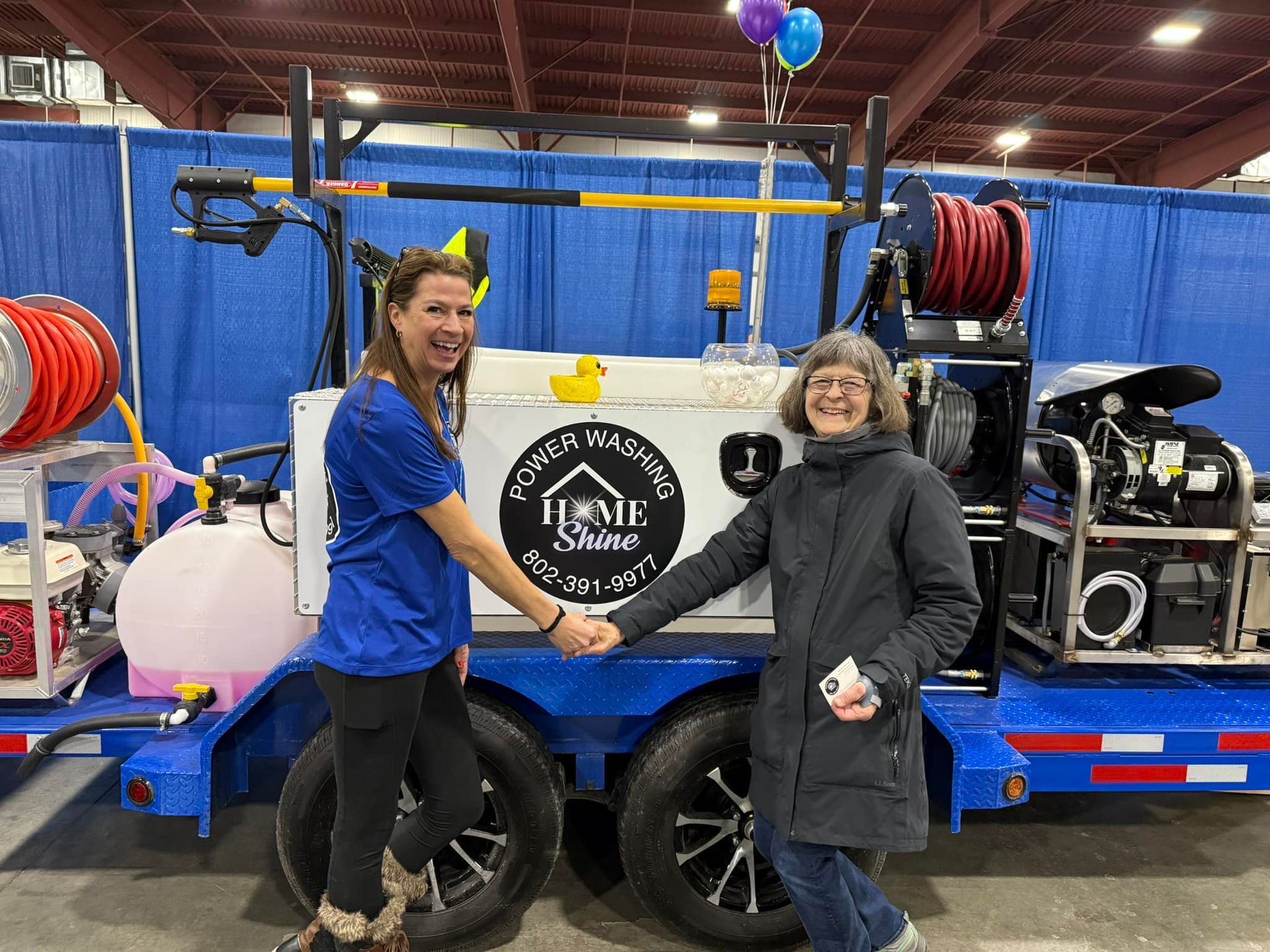 Two women are shaking hands in front of a trailer.