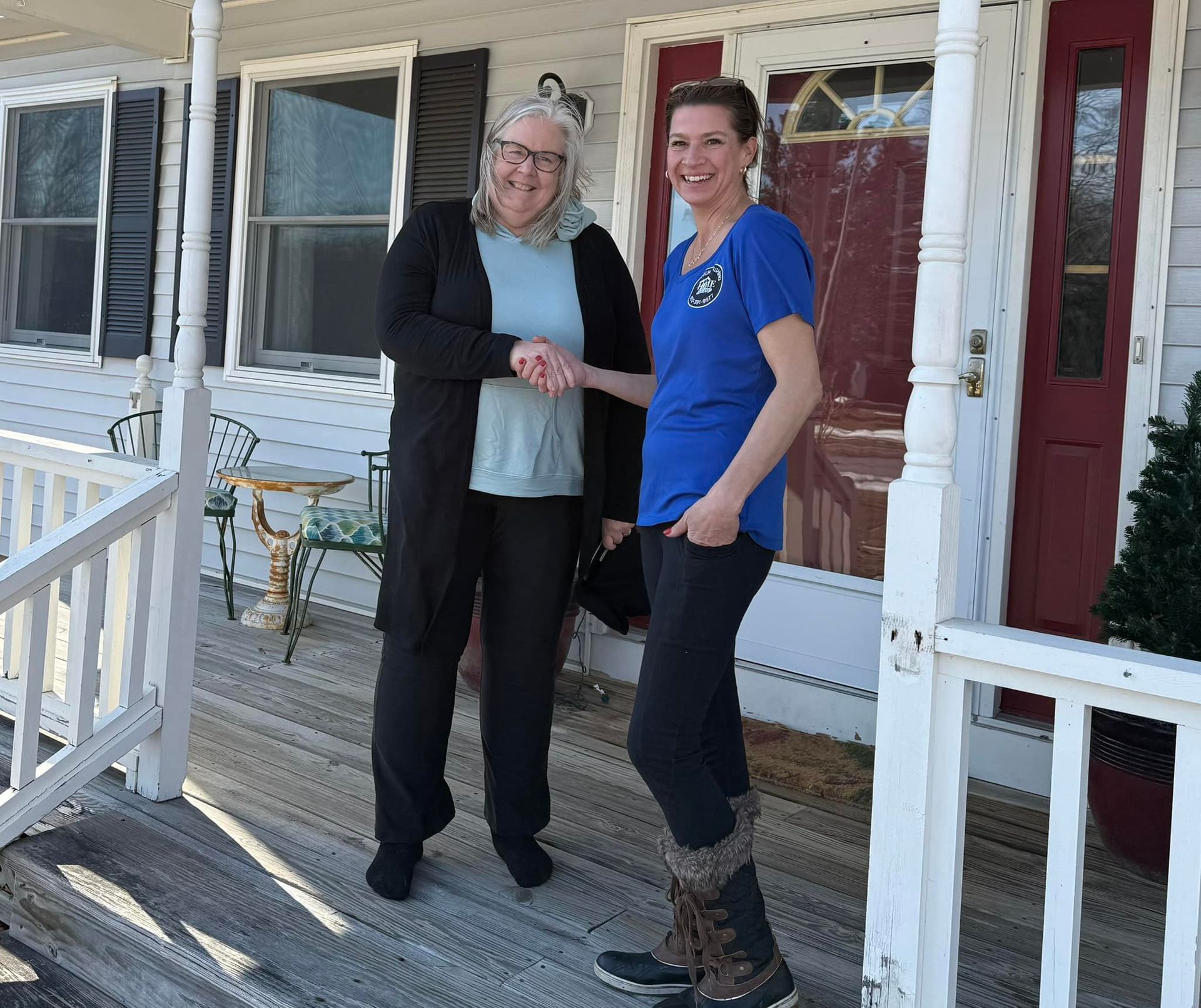 Two women shaking hands on a porch in front of a house