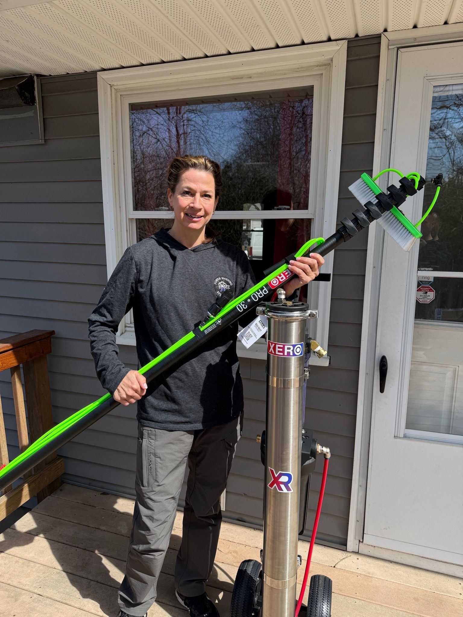 A Home Shine Technician is standing in front of a house holding a green pole.