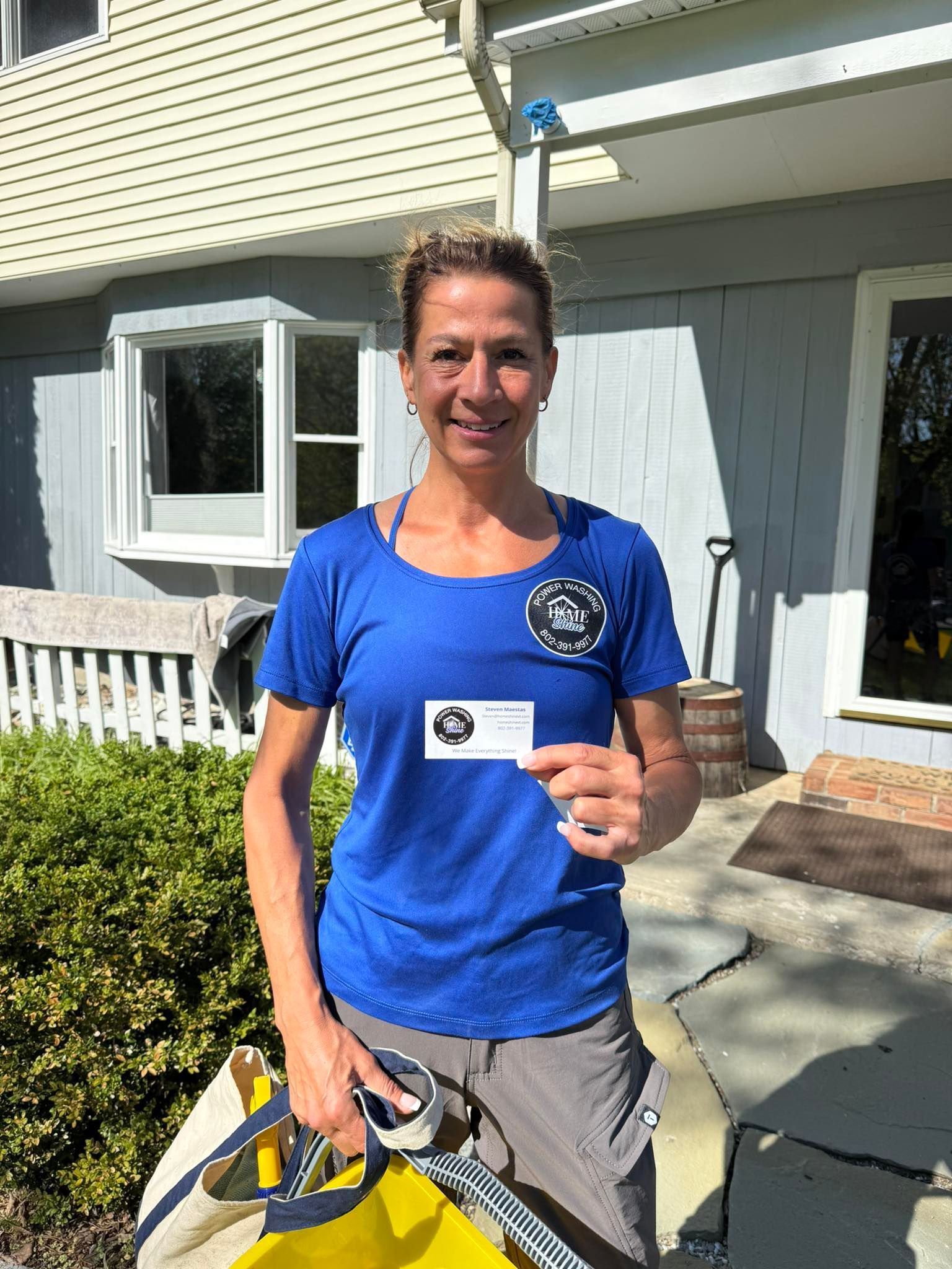 A Home Shine Employee in a blue shirt is holding a card in front of a house.