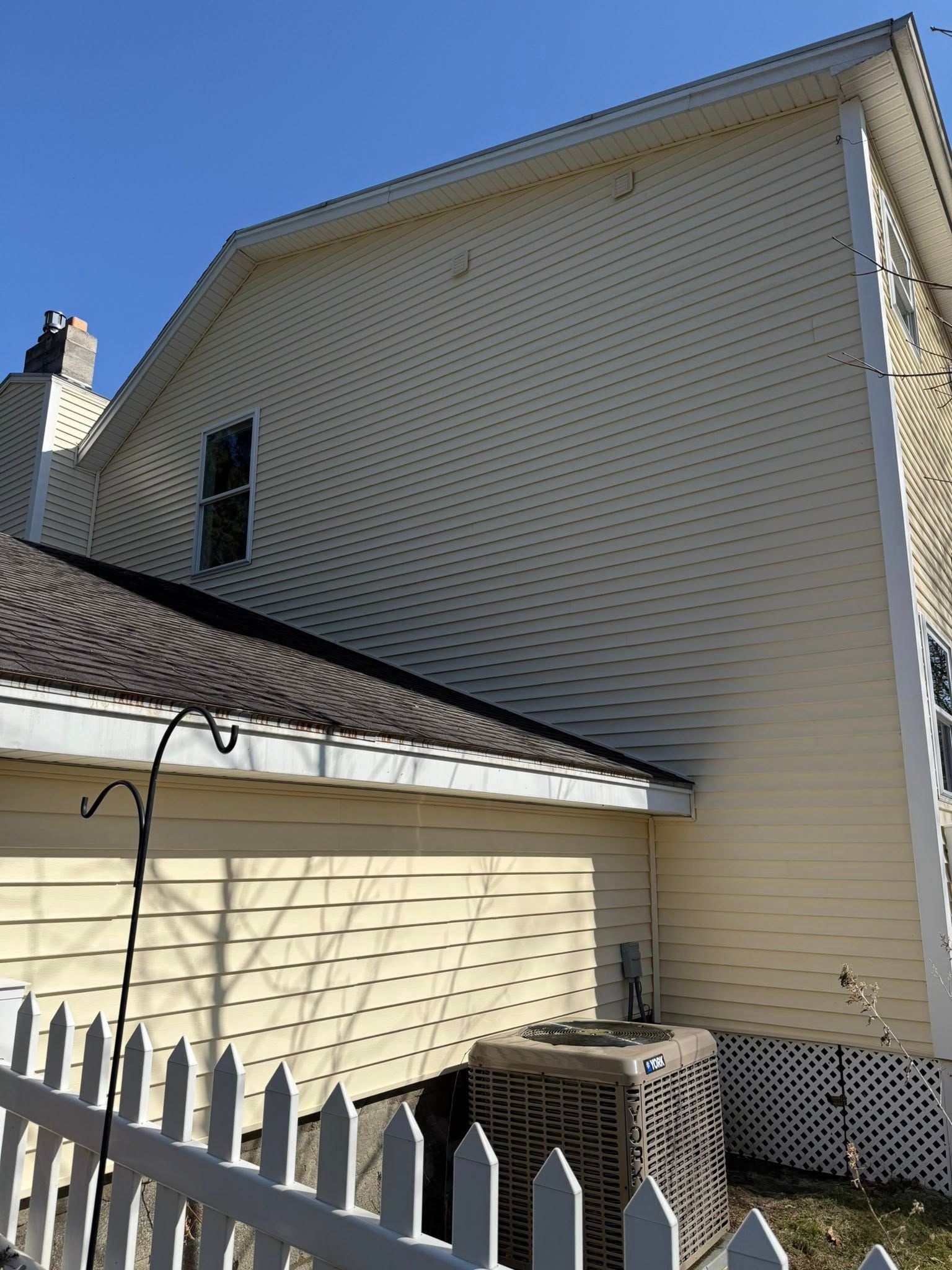 The back of a house with a white picket fence and an air conditioner.