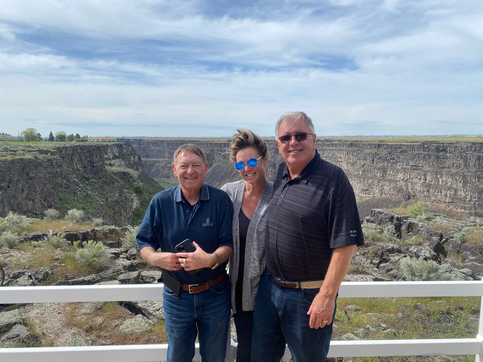 Three people are posing for a picture on a bridge overlooking a canyon.