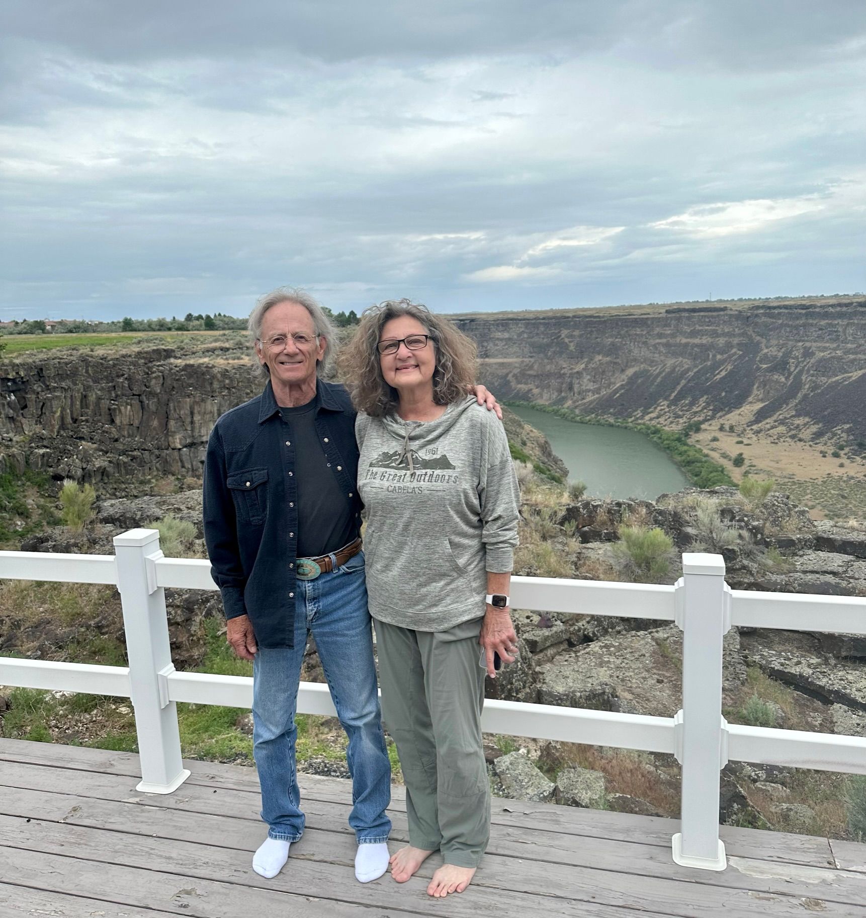 A man and a woman are standing next to each other on a bridge overlooking a river.