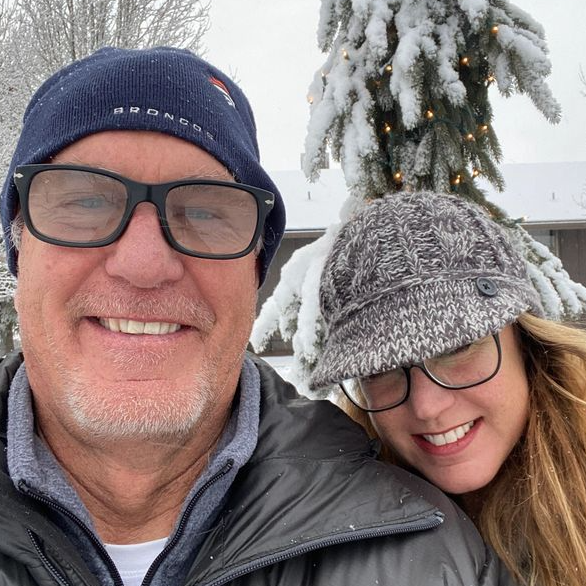A man and a woman are posing for a picture in front of a snowy tree