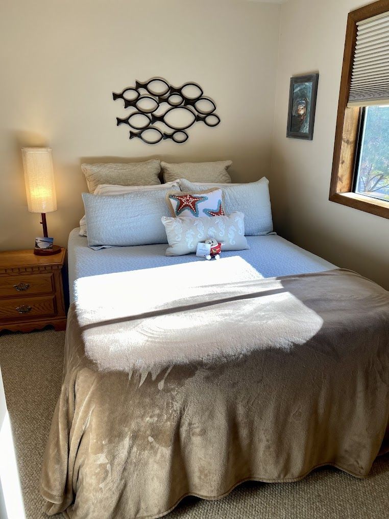 A bedroom with a bed , nightstand , lamp and window.