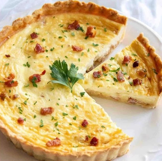 A quiche with a slice taken out of it is on a white plate.