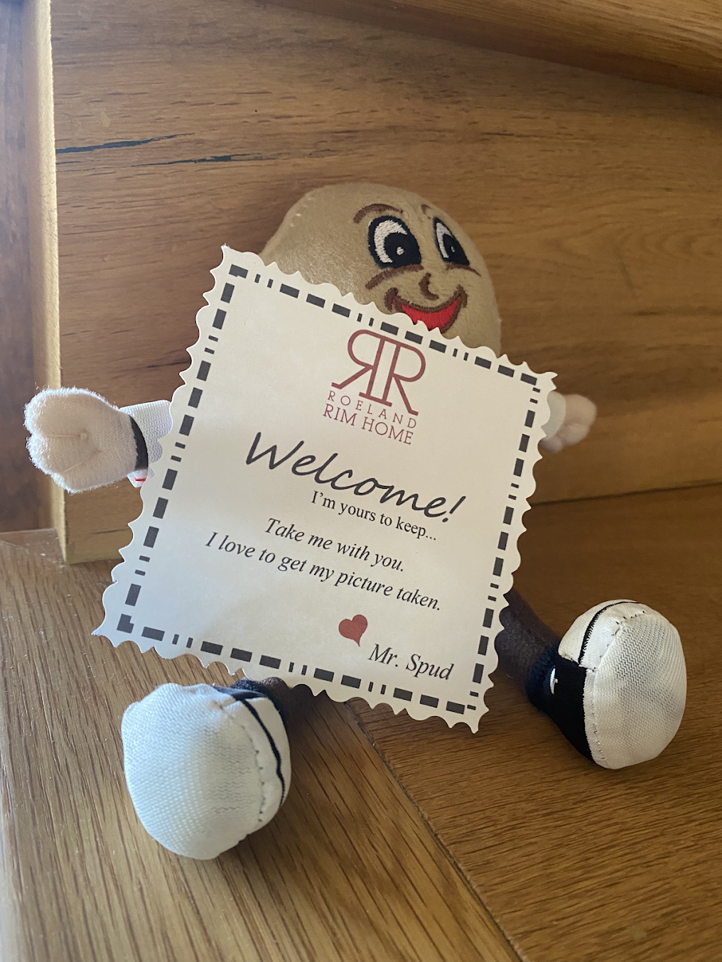 A stuffed potato holding a welcome sign on a wooden table.