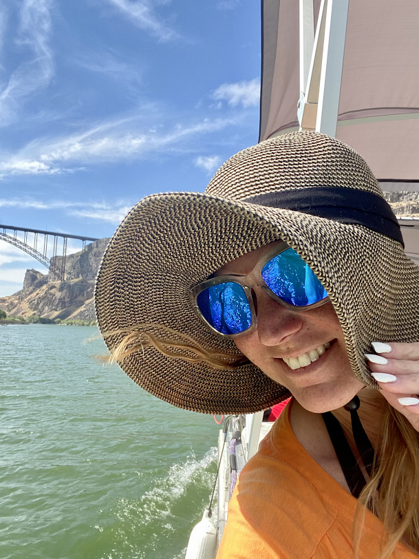 A woman wearing a hat and sunglasses is sitting on a boat.
