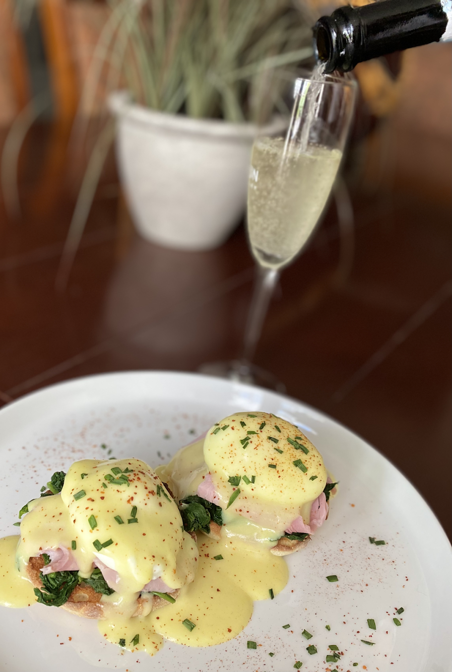 A person is pouring champagne into a glass next to a plate of food.