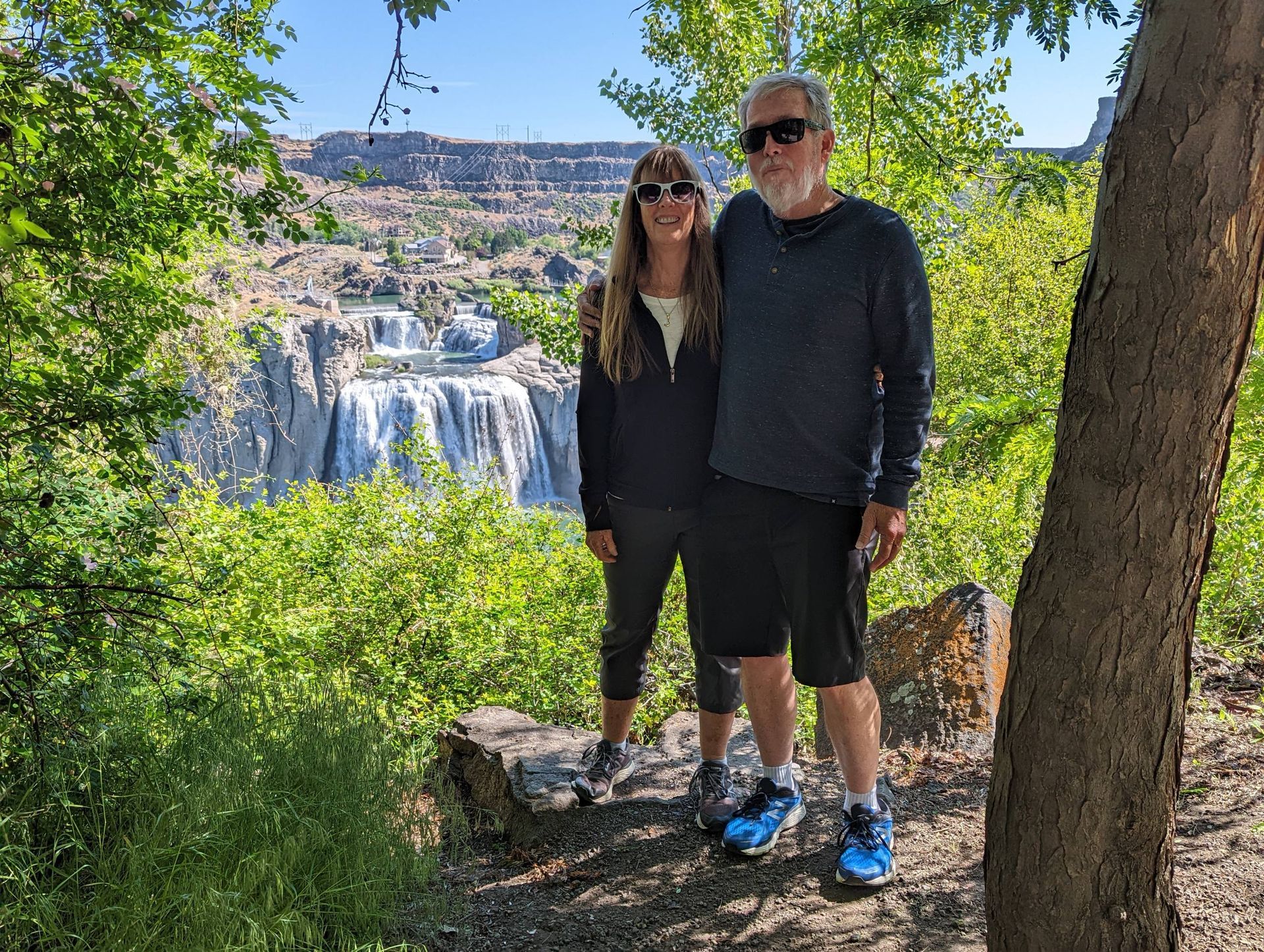 A man and a woman are posing for a picture in front of a waterfall.