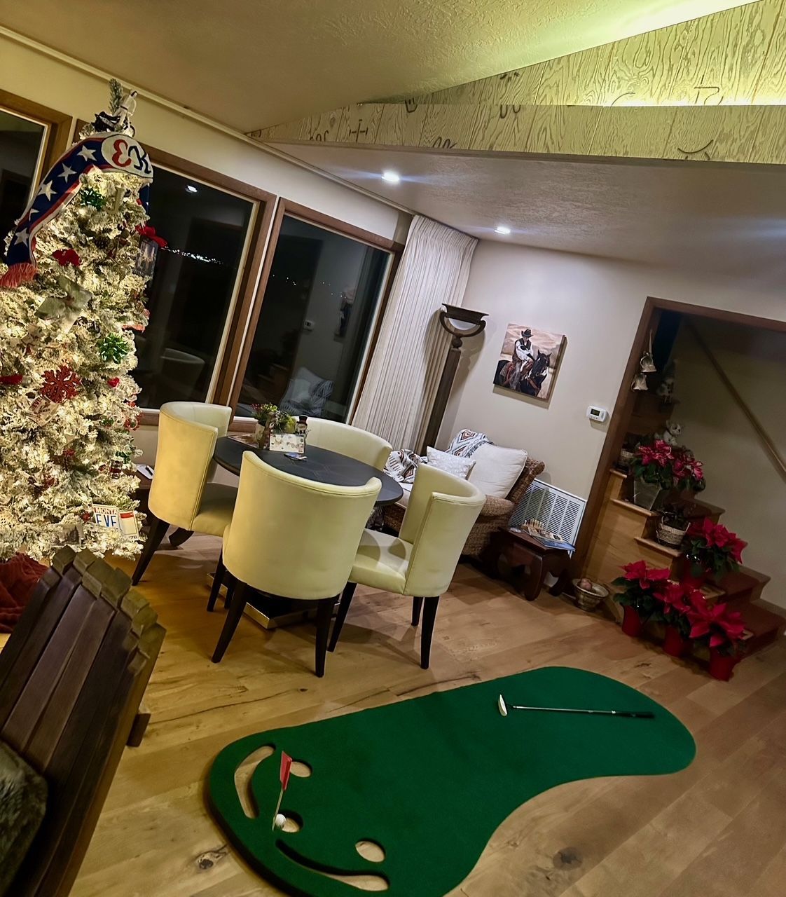Living room with Christmas tree, putting green, dining table, and poinsettias.