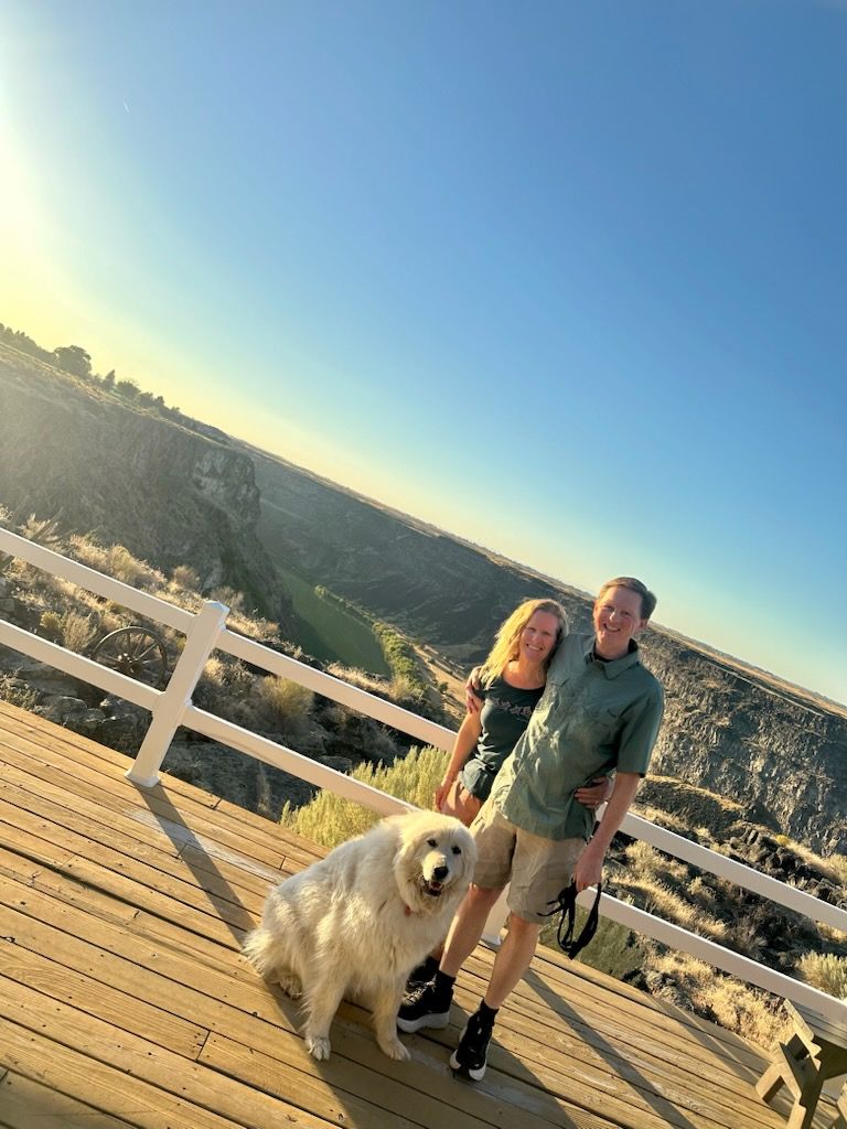 Couple and fluffy white dog posing on a deck with a scenic canyon view in the background.