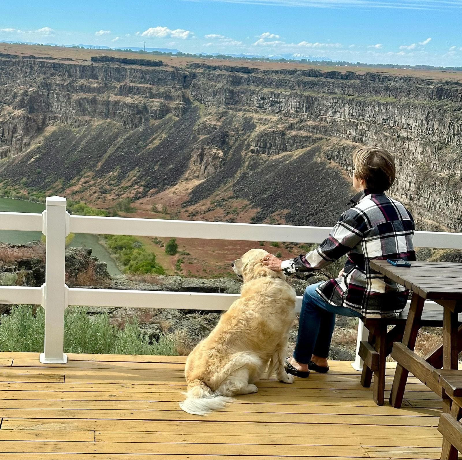 Woman and golden doodle dog on wooden deck overlooking canyon with blue sky.