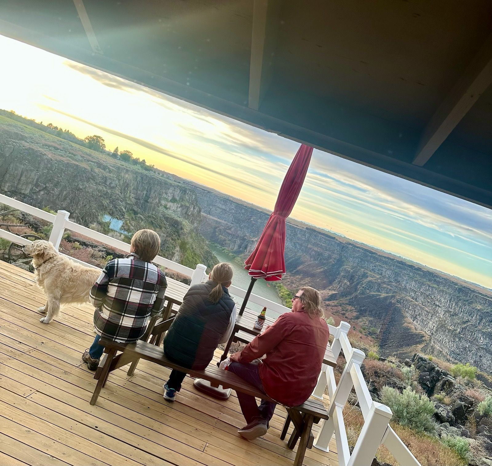 Family on deck overlooking a canyon. Golden retriever stands nearby. Sunset sky.