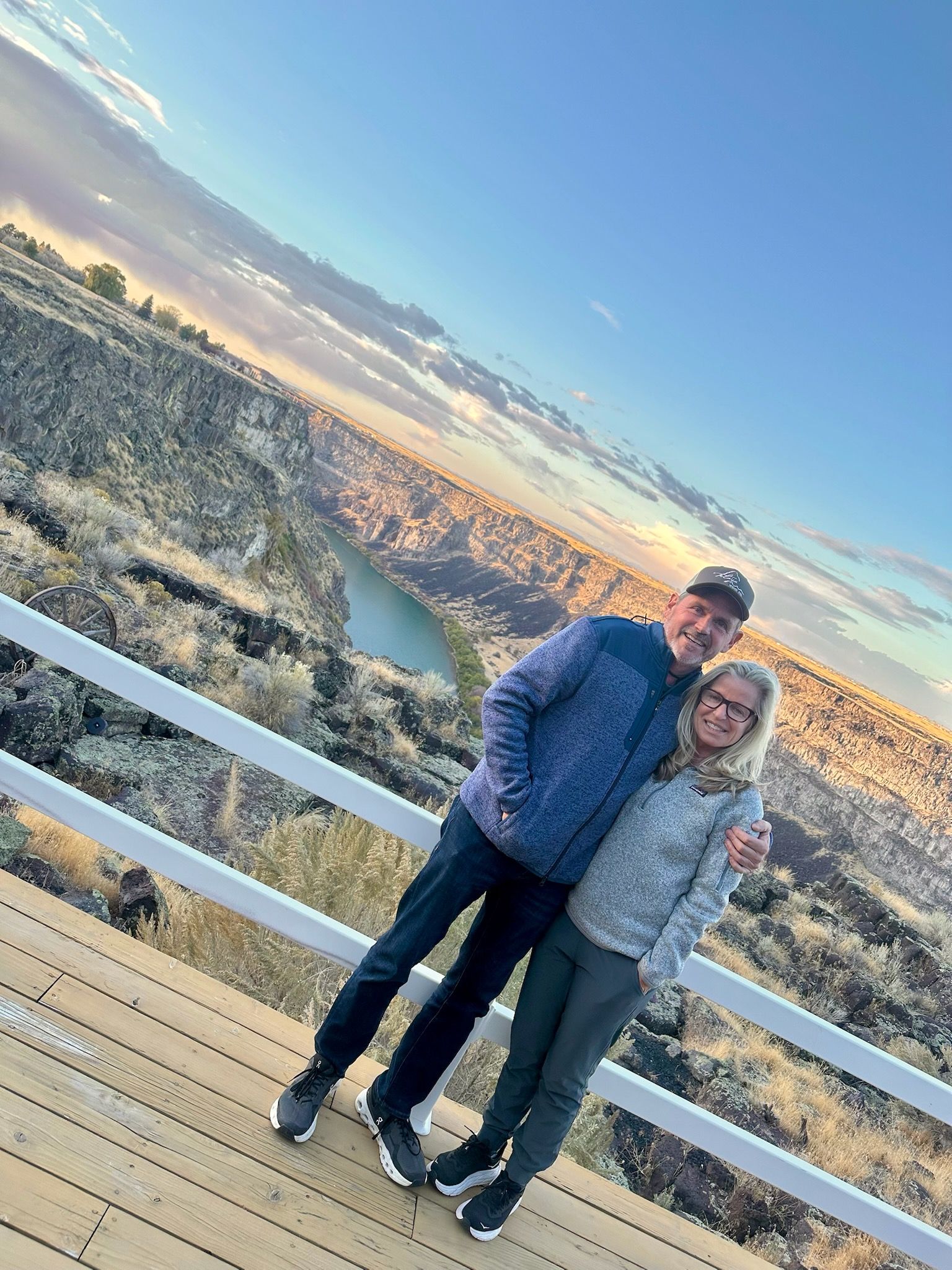 Couple on a wooden bridge with a canyon and colorful sunset in the background.