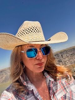 Woman in cowboy hat and sunglasses, looking up at sunny sky, outdoors.