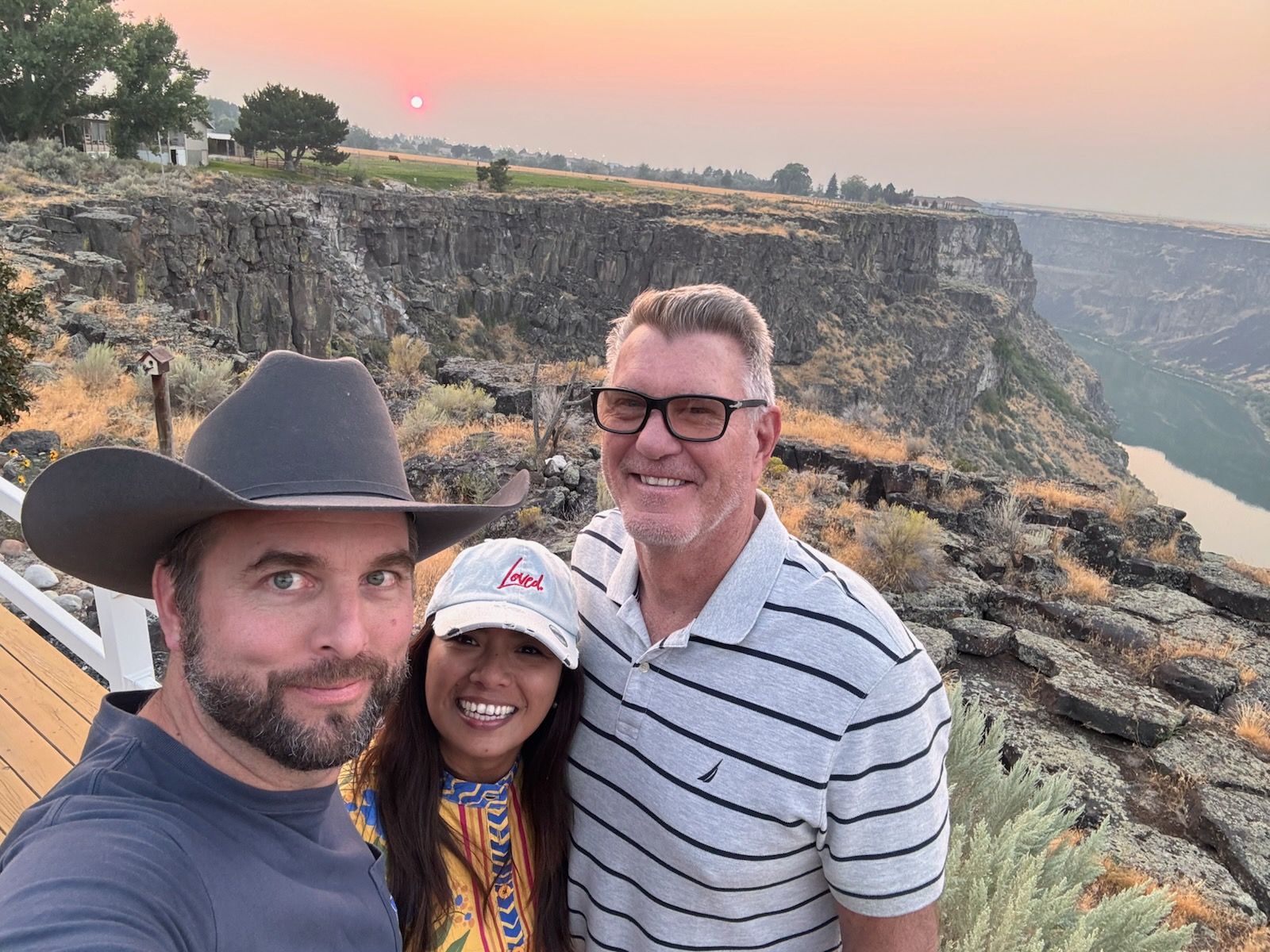 Three people posing for a selfie at sunset near a canyon.