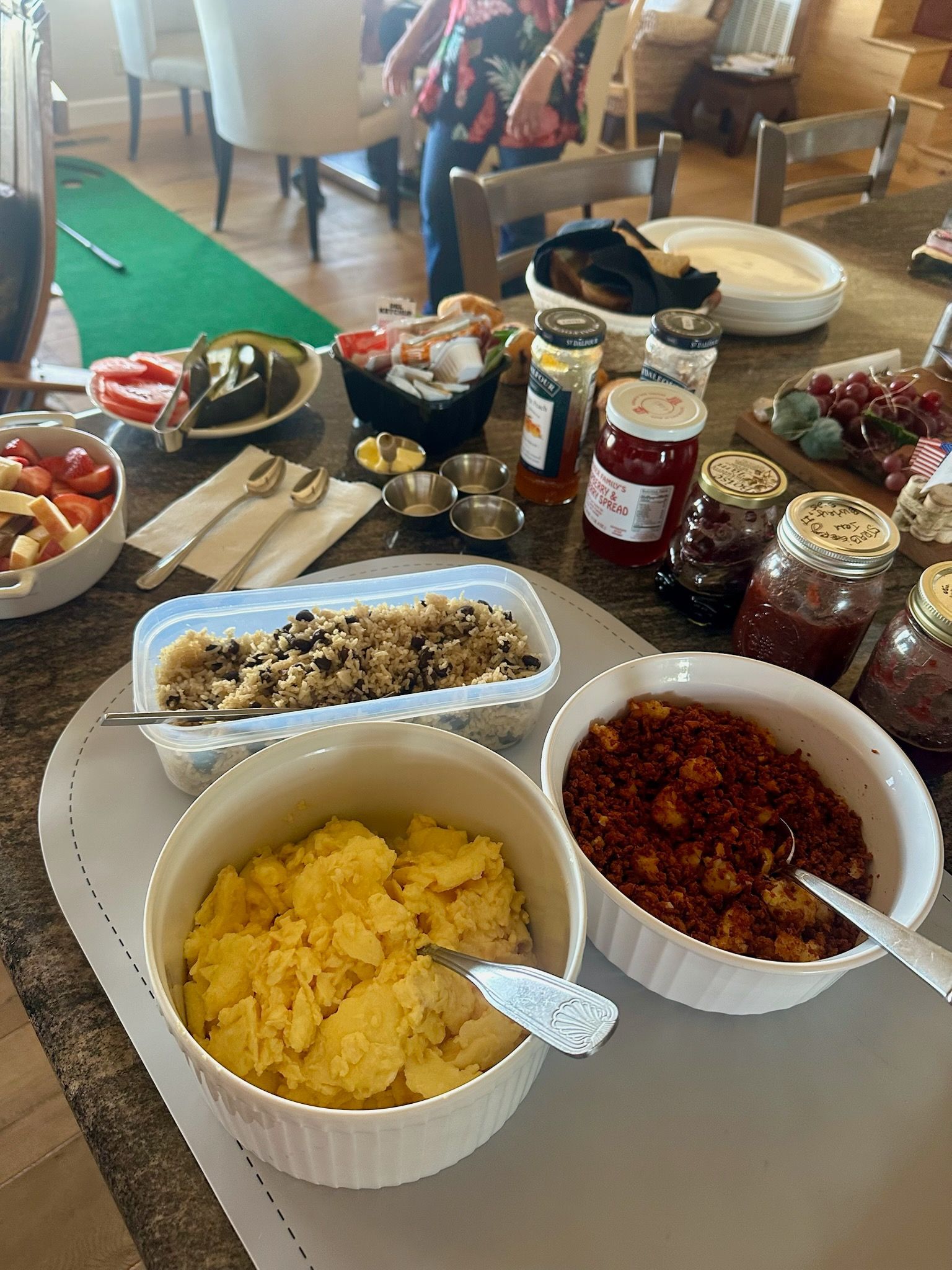 A buffet table with bowls of food like scrambled eggs, fruit, and jams.