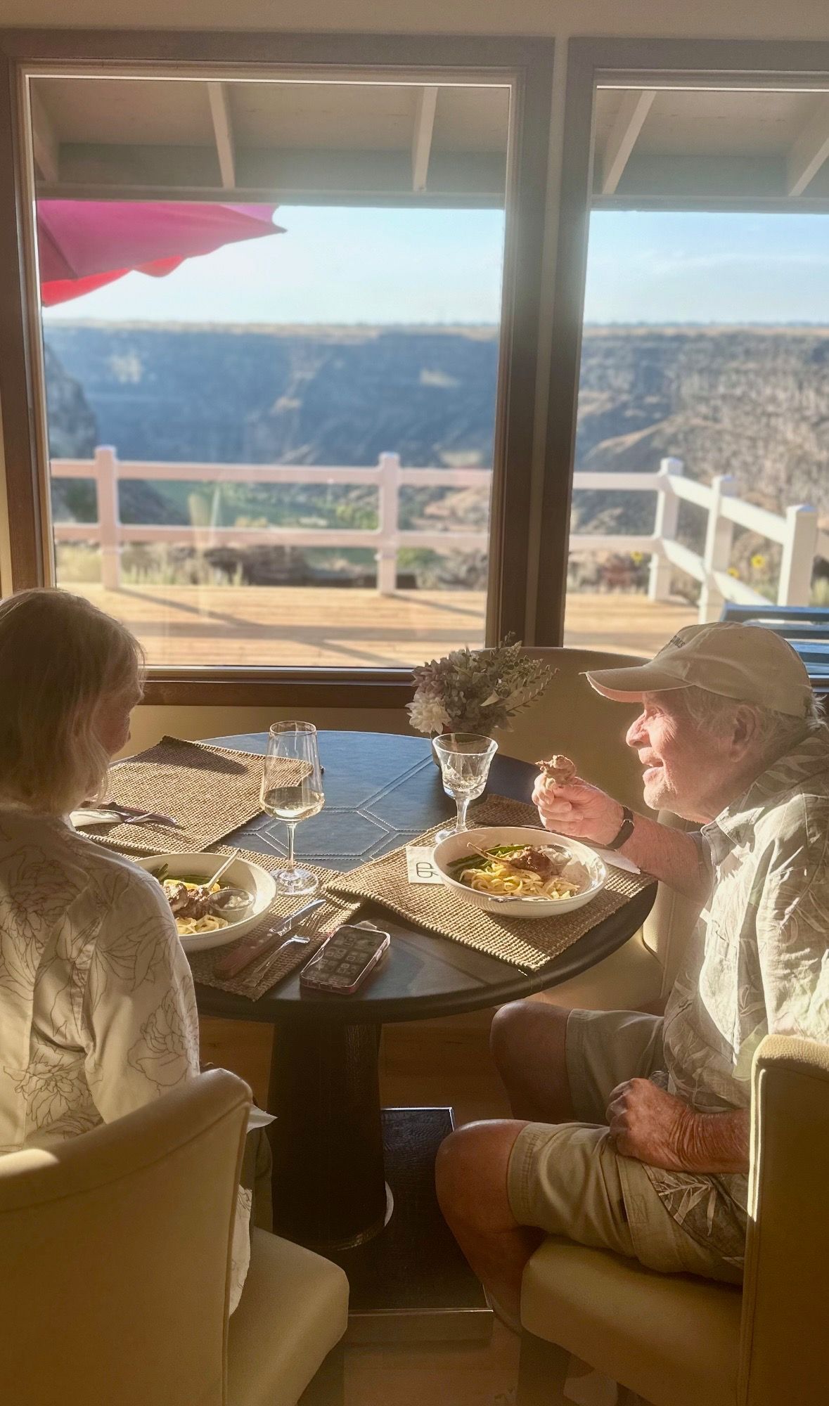 Two people eating at a table near a window overlooking a canyon.