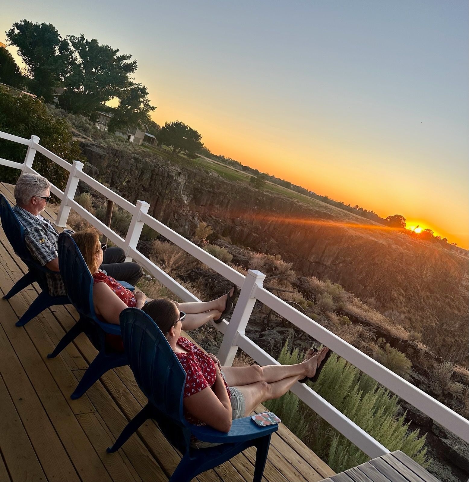 A group of people sitting on a deck watching the sunset