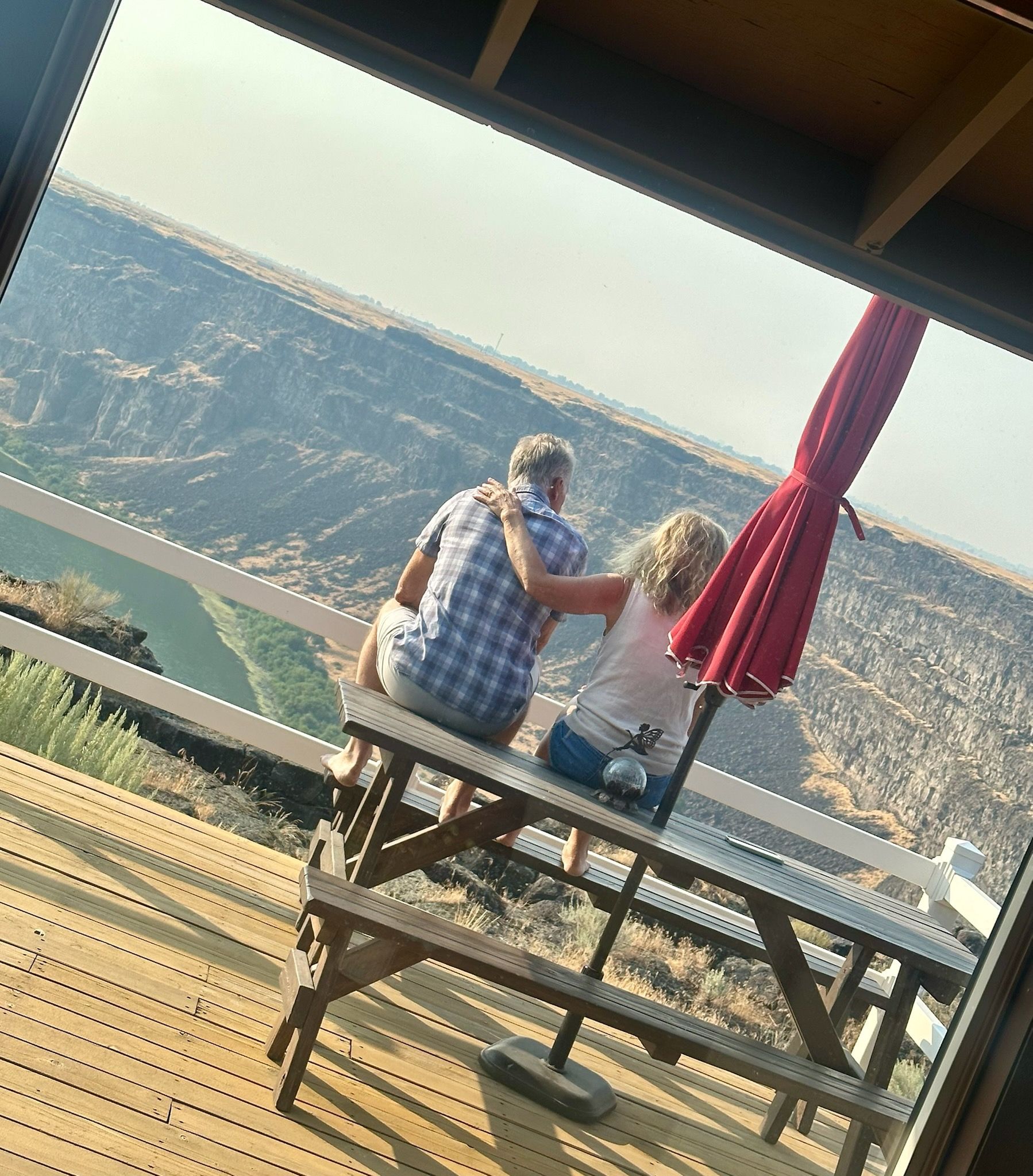 Couple hugging on a bench overlooking a canyon, red umbrella to the right.