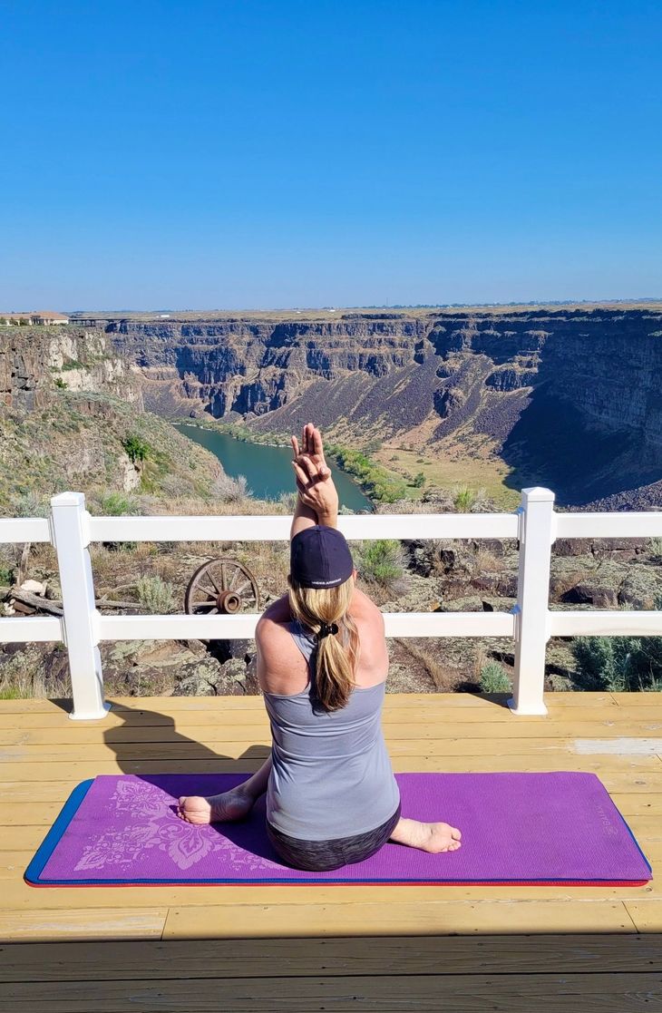 Person doing yoga on a purple mat overlooking a canyon under a clear blue sky