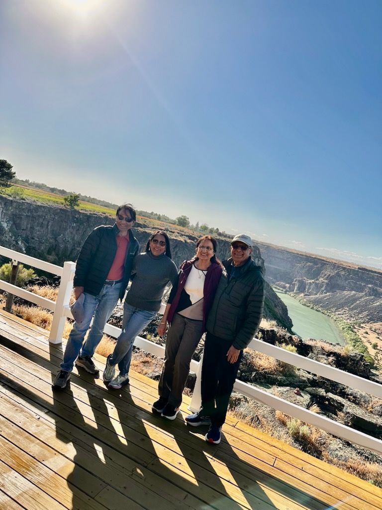 Four people standing on a wooden deck overlooking a canyon under a bright blue sky