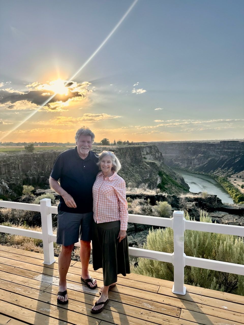 Couple on a wooden deck, looking at a canyon at sunset, with river below.