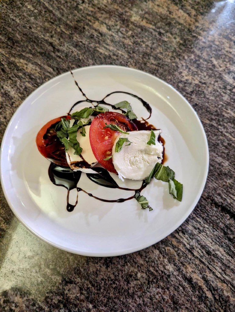A white plate topped with a tomato , mozzarella and balsamic sauce.