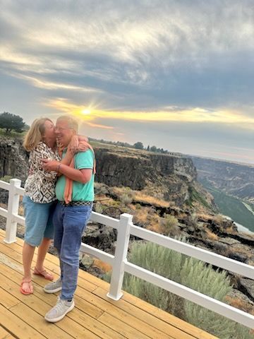 Couple hugging and kissing on a wooden deck overlooking a canyon at sunset.