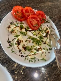 Caprese salad: sliced tomatoes and mozzarella, drizzled with balsamic glaze and herbs on a white plate.