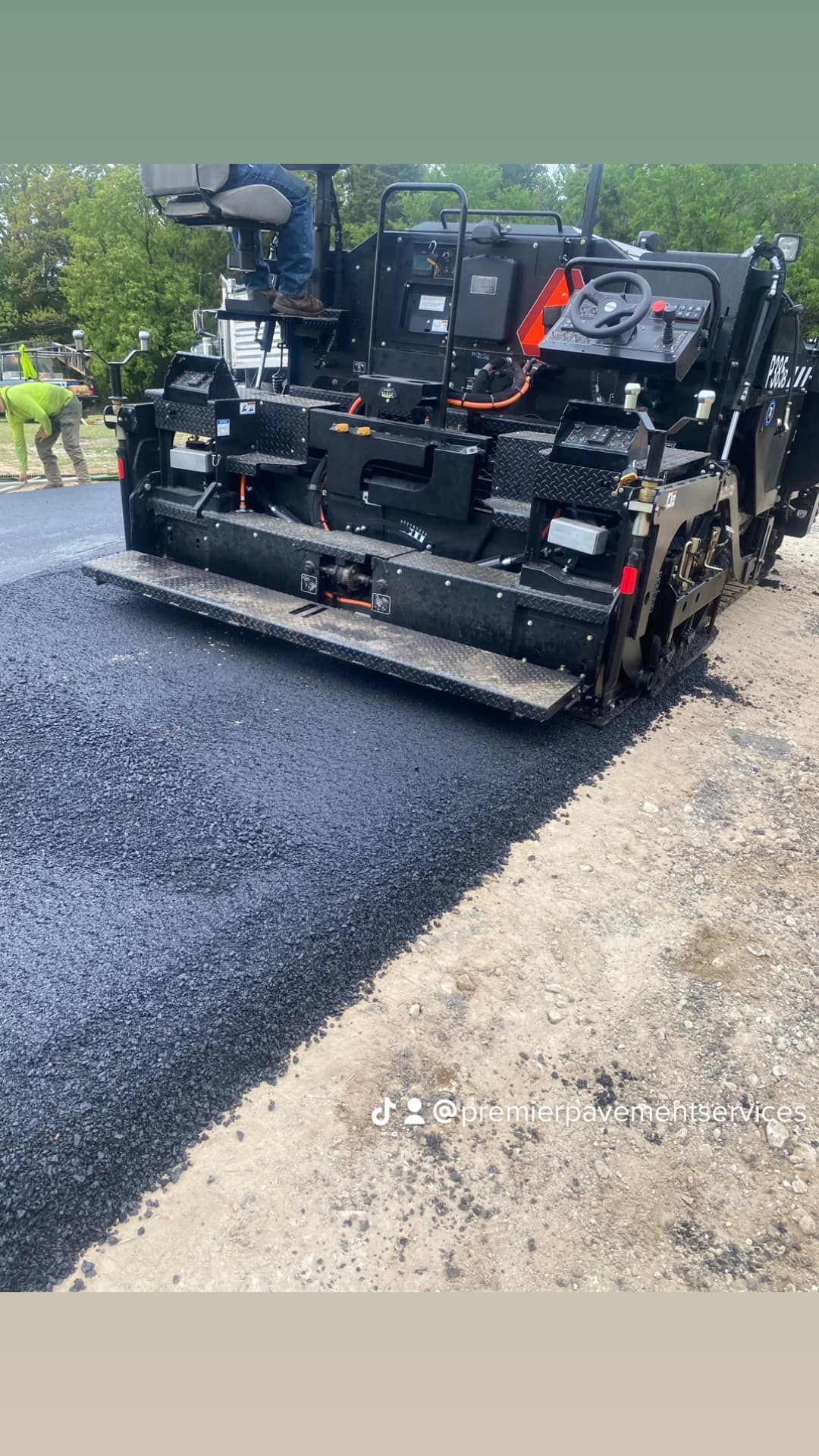 A machine is laying asphalt on the side of a road.