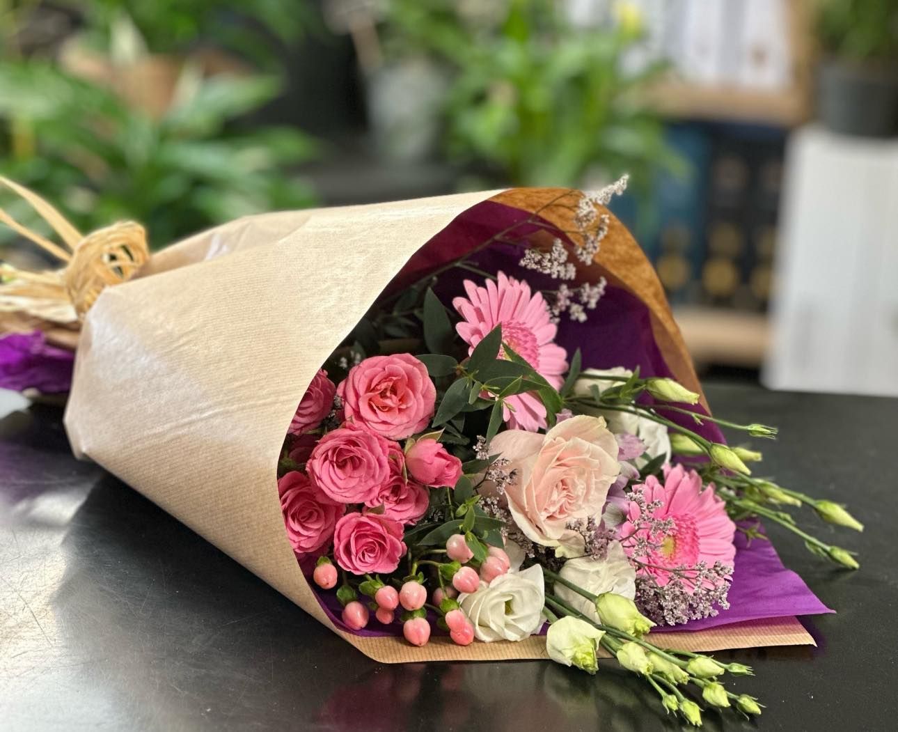 Bouquet of pink and white flowers wrapped in brown paper, on a dark table.