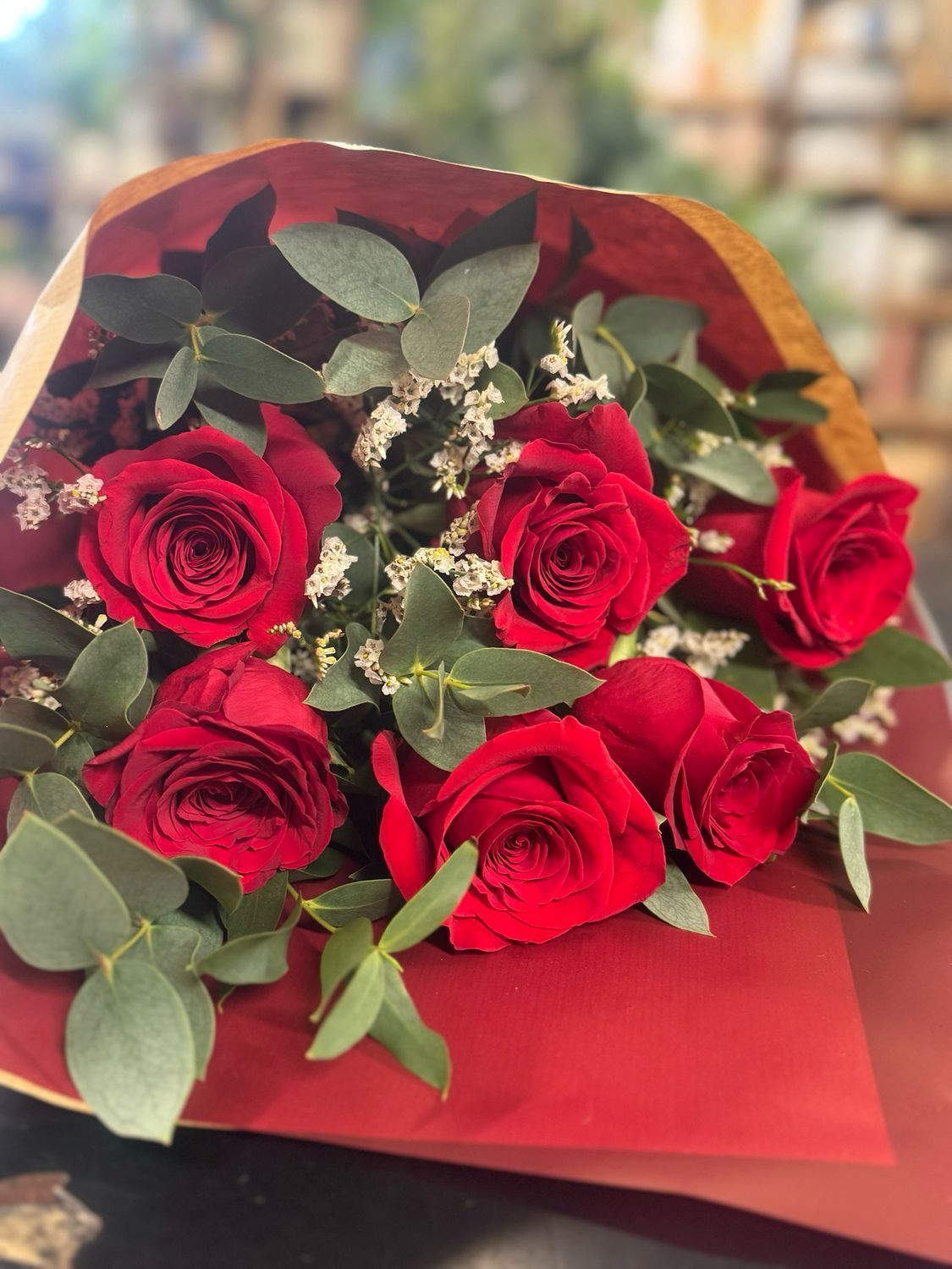 Bouquet of red roses with green eucalyptus leaves wrapped in red and brown paper.