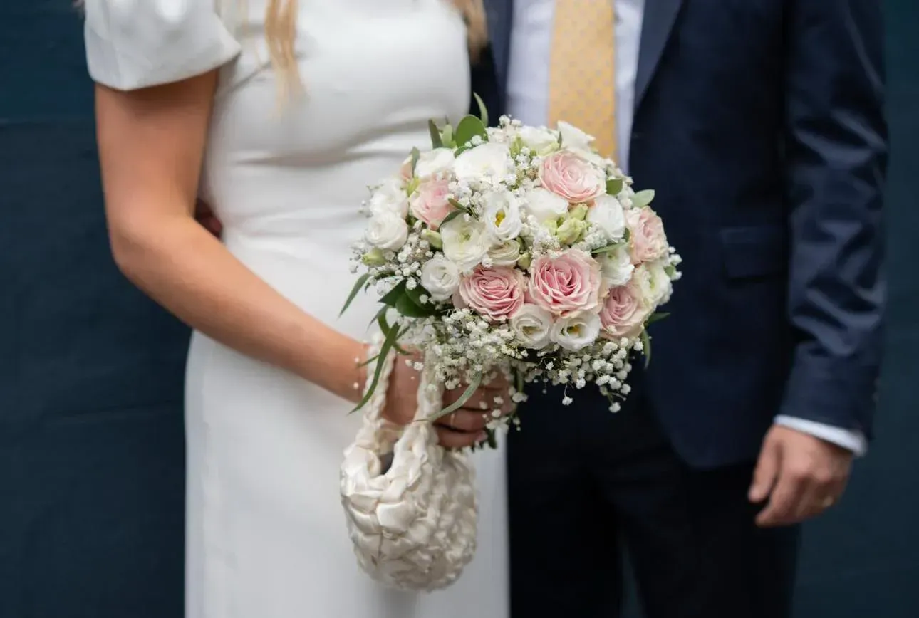 Bride in white dress holding floral bouquet next to a person in a navy suit.