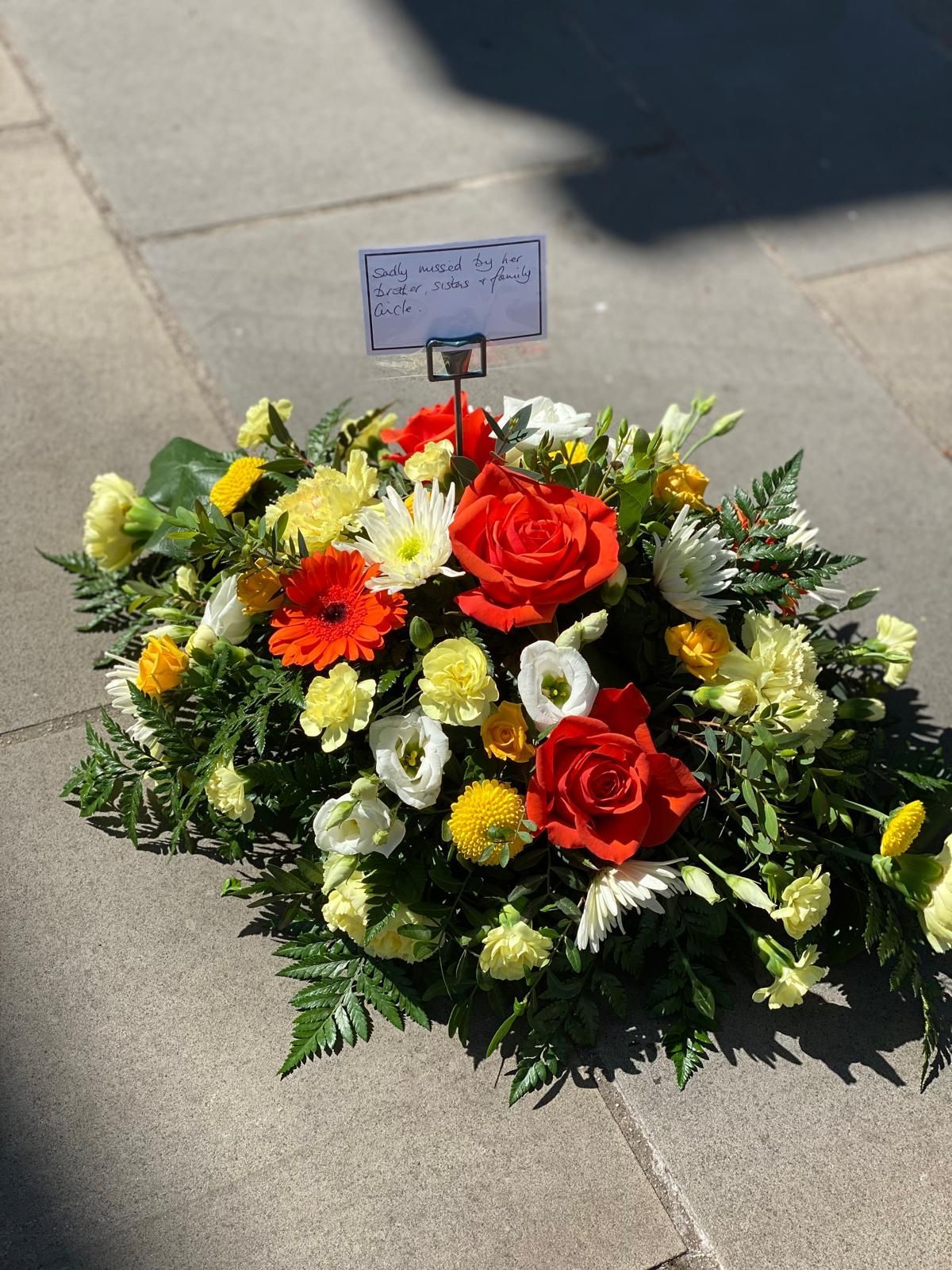 Floral arrangement with red roses, yellow and white flowers, and a small card on a stone surface.