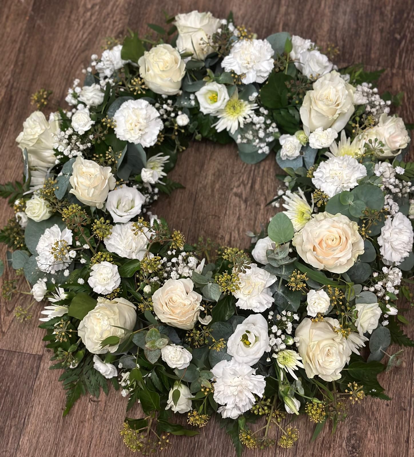 White floral wreath with roses, carnations, and greenery.